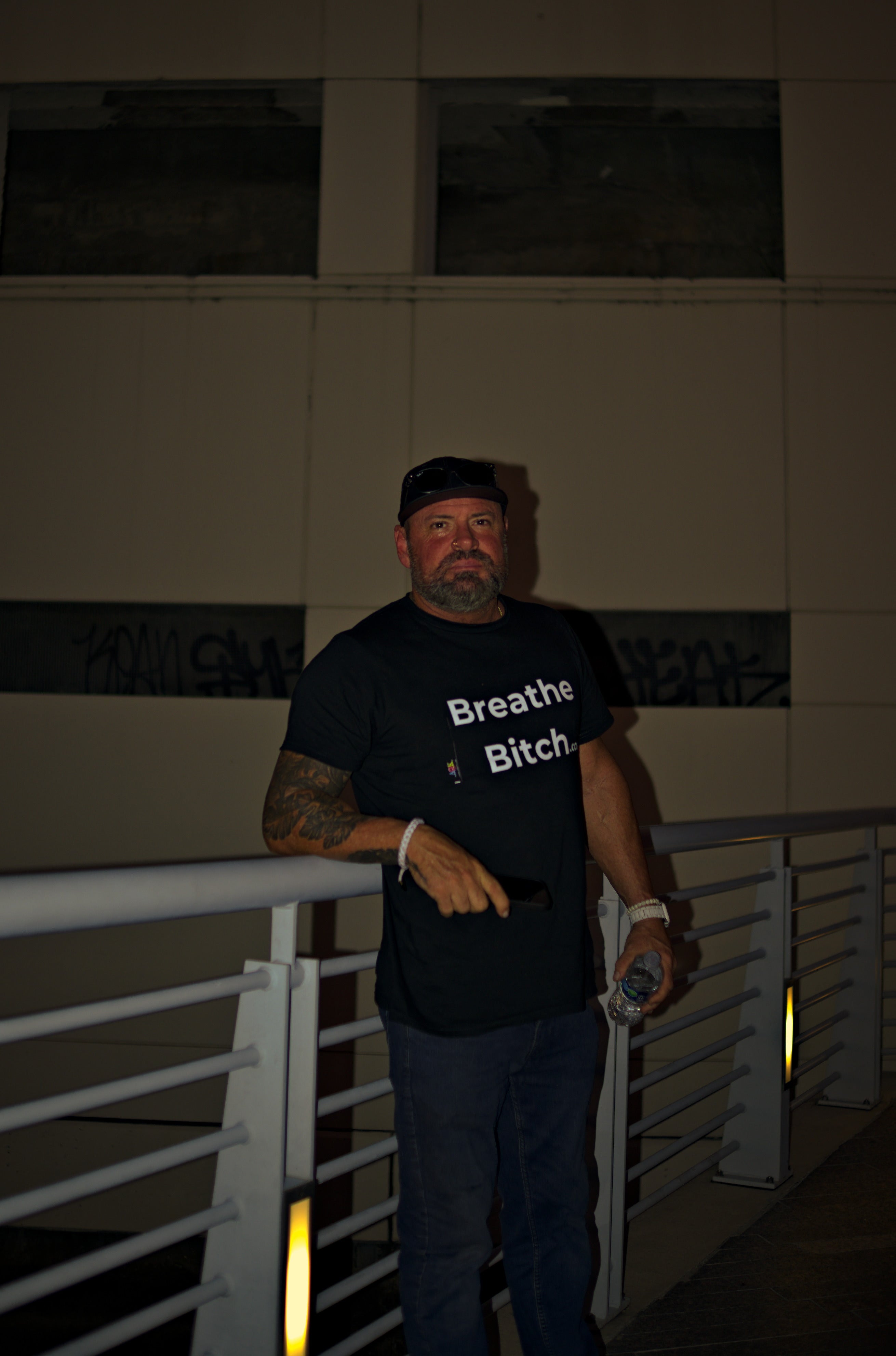 Man wearing a black t-shirt with text, standing against a dark background. Acacia Cinematography, Tampa, Fl 