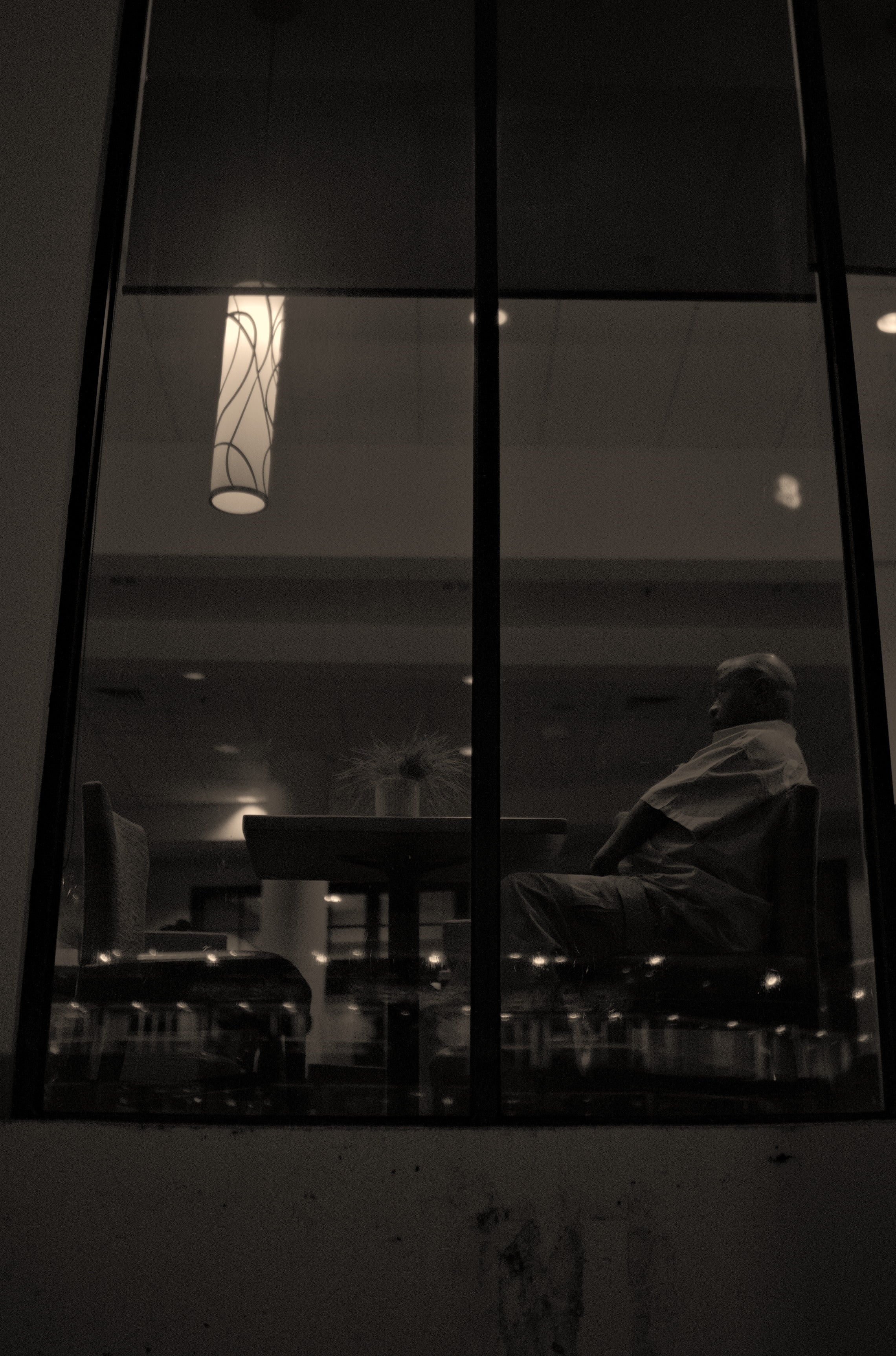 Person sitting at a table in a dimly lit room, viewed through glass. Acacia Cinematography, Tampa, Fl 